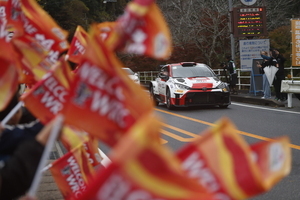 沿道から旗を振る観客とラリーカー